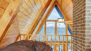 A loft bedroom with a sloped ceiling, wooden beams, a large window, and a bean bag chair.