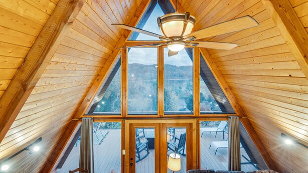A high-ceilinged wooden room with a large window and a ceiling fan.
