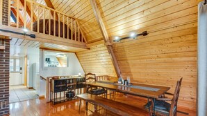 A cozy cabin interior with a wooden dining table, chairs, a kitchen area, and a loft space with a view.