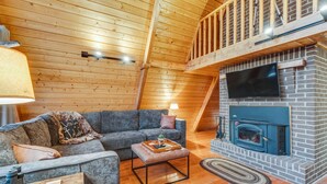A cozy loft-style living room with a wooden ceiling, a fireplace, a sofa, and a television.