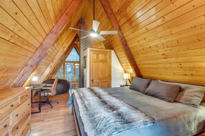 A cozy attic bedroom with a sloped ceiling, wooden walls, a bed, a desk, and a chair.