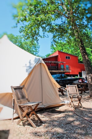 A tent set up in a natural setting with a red building in the background. - Son's Guadalupe Glamping Tent A (New Braunfels)