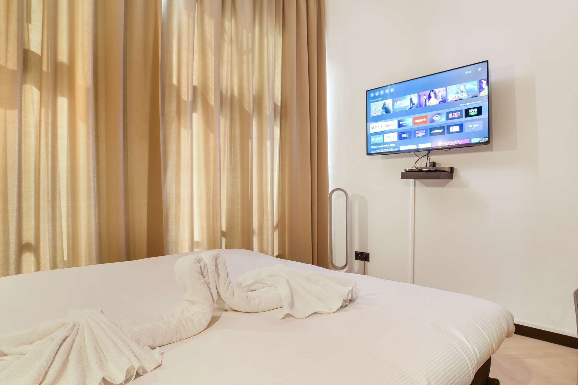 A hotel room with a bed, a TV mounted on the wall, and a curtain.