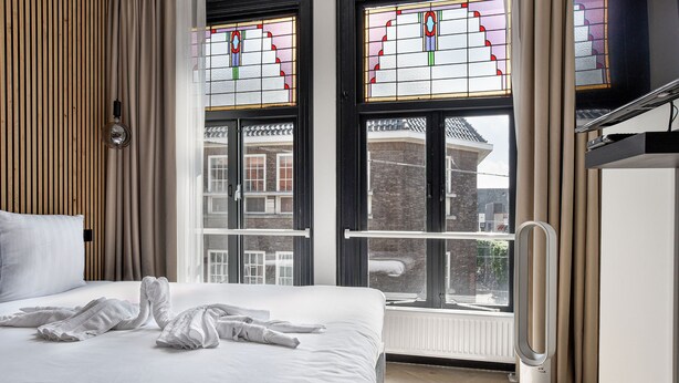 A hotel room with a bed, a radiator, and a window with stained glass. - Haarlem Apart Hotel (Haarlem)