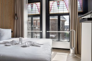 Ett hotellrum med en säng, ett element och ett fönster med målat glas.
