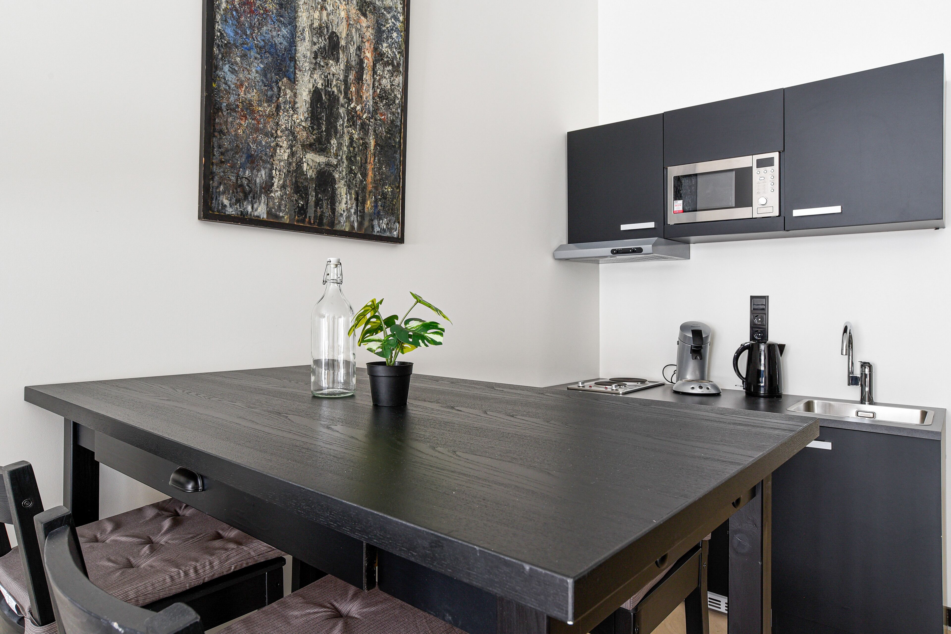 Een moderne keuken met een donker aanrecht, een magnetron, een koffiezetapparaat en een spoelbak.