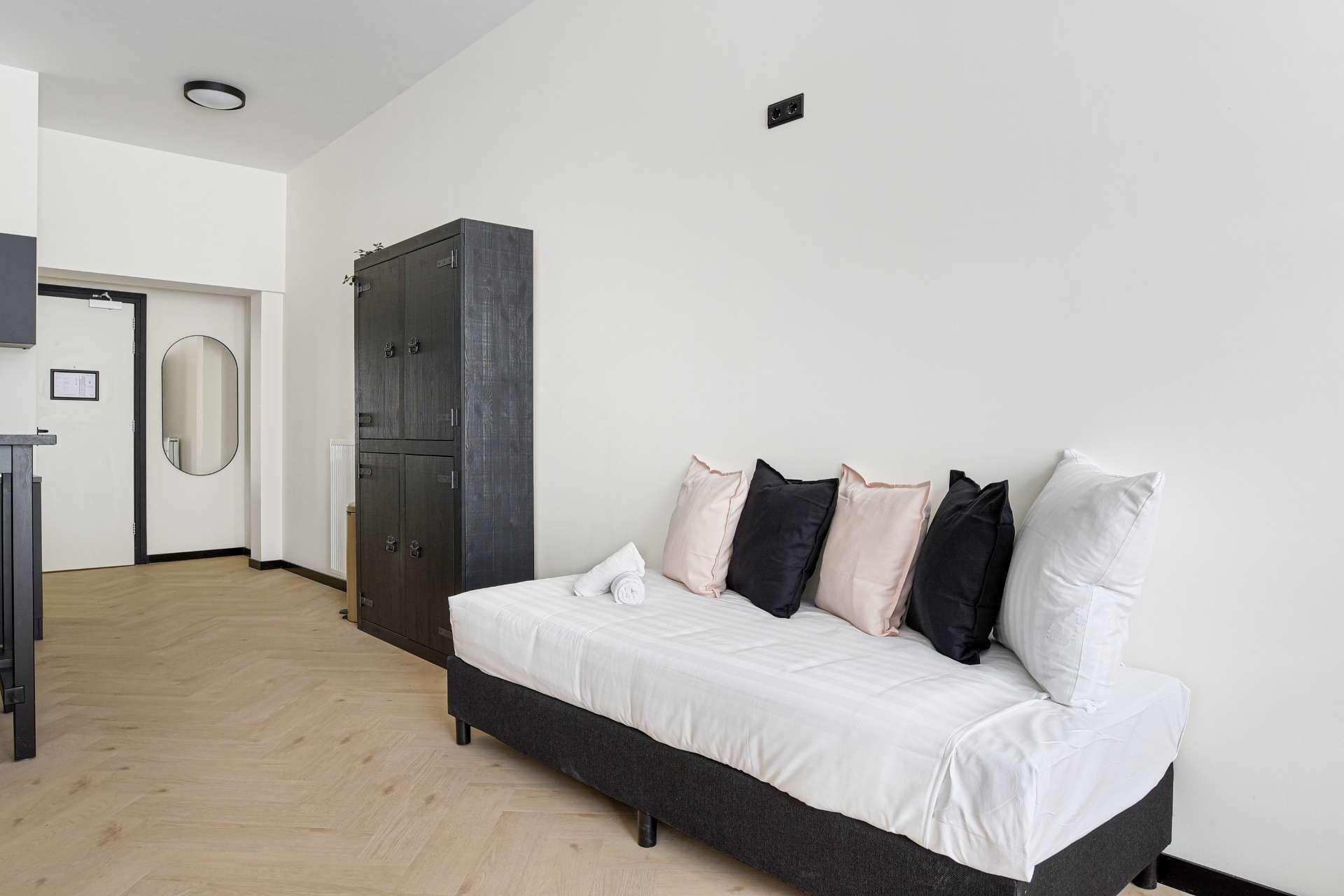 A bedroom with a bed, a wardrobe, a mirror, and a door.