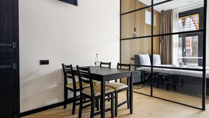 A modern dining area with a wooden table and chairs, a glass partition, and a view of the city through large windows. - Haarlem Apart Hotel (Haarlem)