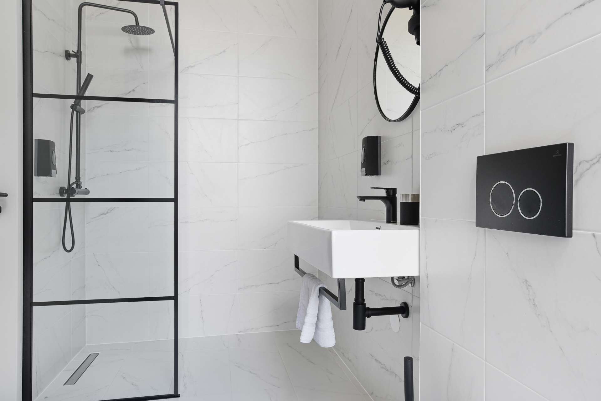 Un baño moderno con ducha de vidrio, un lavabo blanco con grifo negro y un perchero para toallas.