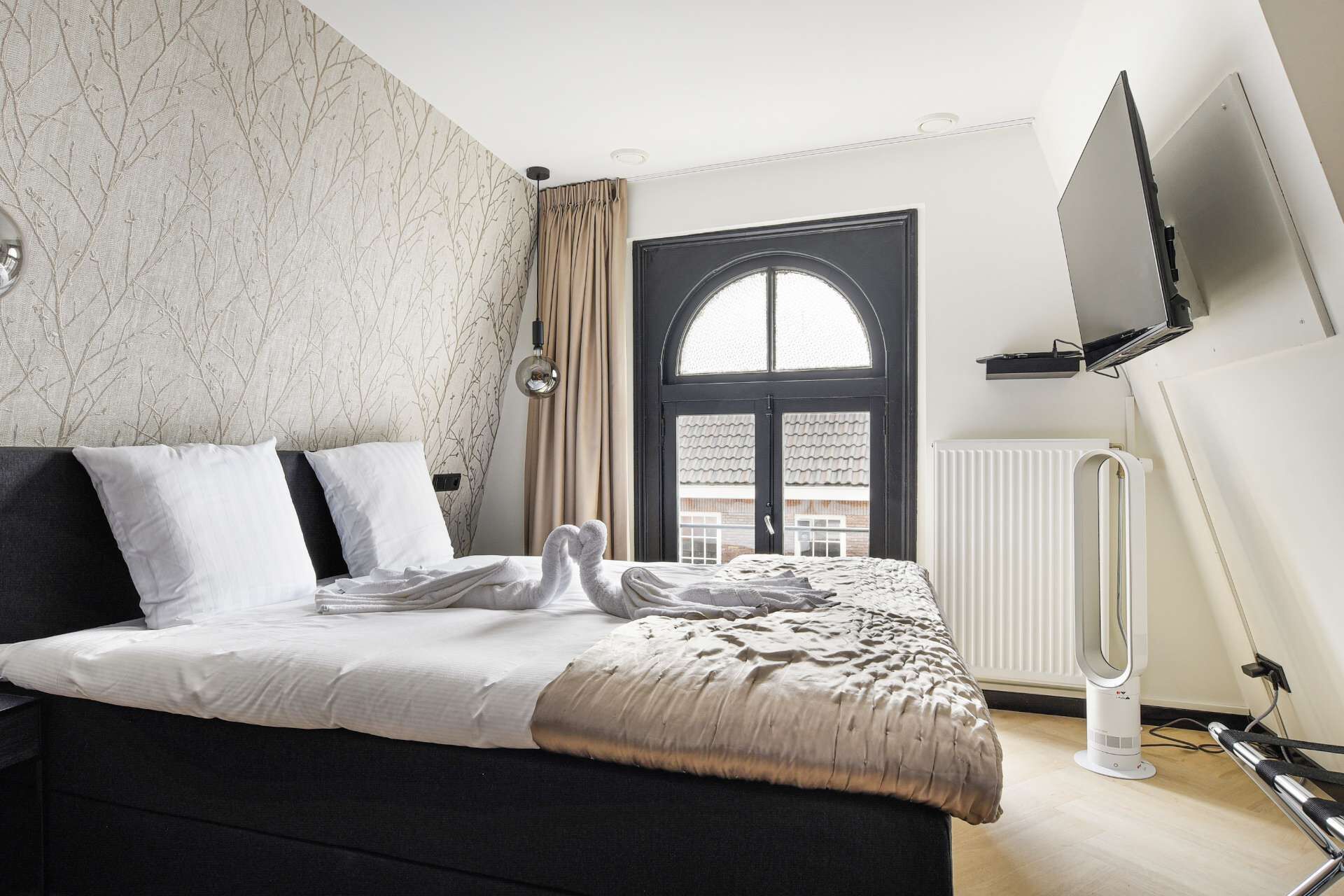 Um quarto moderno com cama, radiador, TV fixada na parede e janela com cortinas.