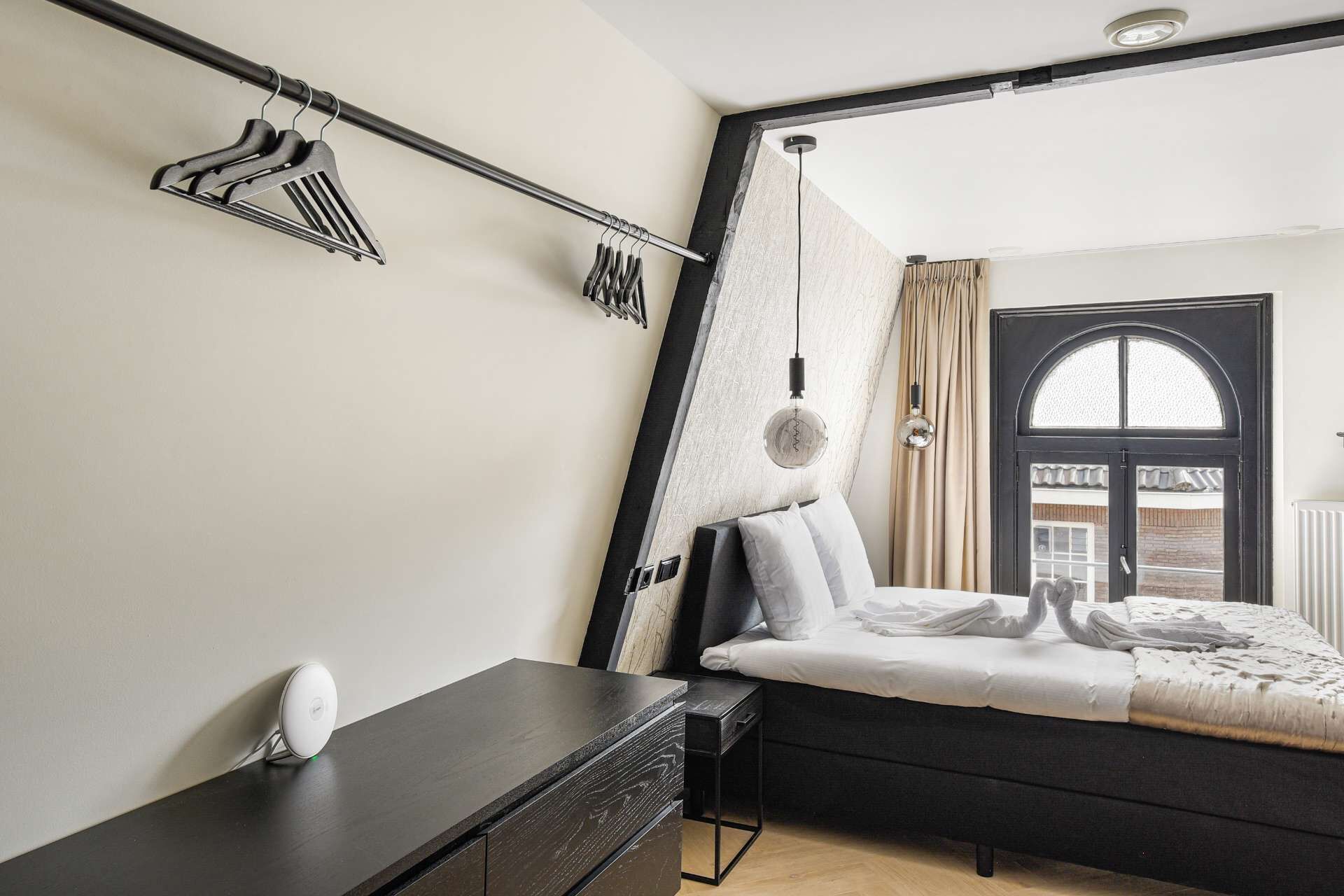 Un dormitorio con cama, escritorio, silla, lámpara colgante y ventana con cortinas.