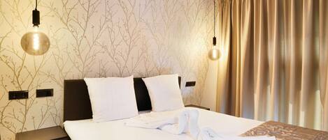 A hotel room with a bed, two bedside tables, a wall with a tree branch pattern, and a window with curtains.