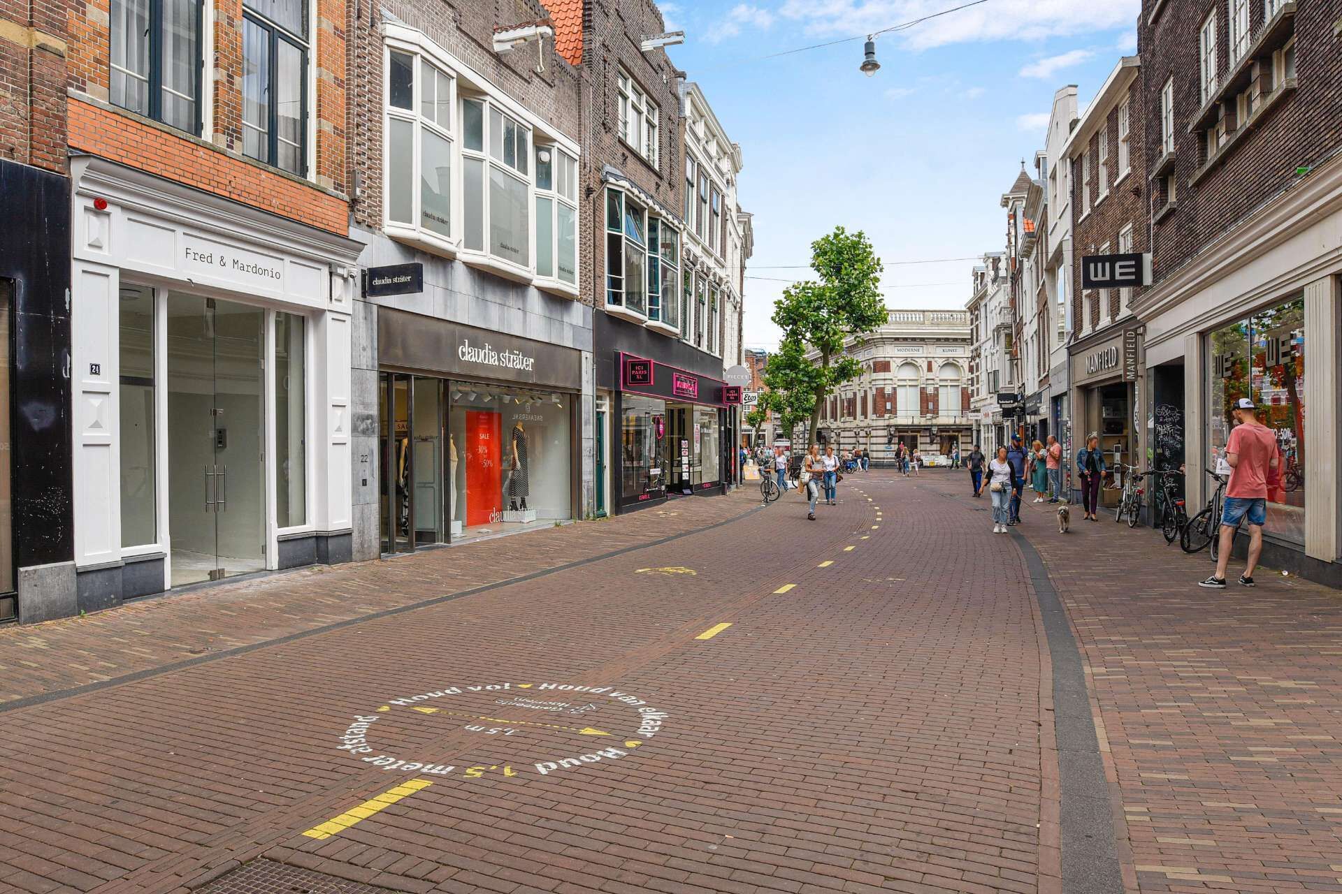 Een voetgangersstraat met winkels en gebouwen, waaronder 'Fred & Mardonio' en 'Claudia Sträter'.