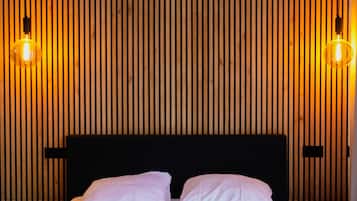 Cama com roupa de cama branca, duas almofadas e cabeceira em frente a parede de ripas de madeira com duas luminárias fixadas na parede.