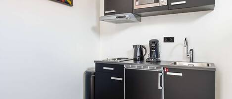 Una cocina compacta con microondas, cafetera y lavamanos.