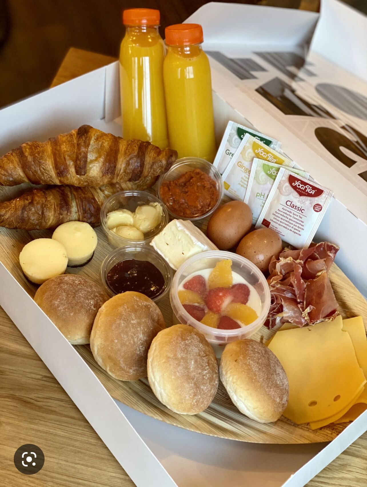 A breakfast tray with croissants, pastries, cheese, eggs, fruit, and beverages.