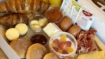 A breakfast tray with croissants, pastries, cheese, eggs, fruit, and beverages.