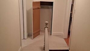 A narrow hallway with white walls and wooden flooring. There are two doors on either side, one of which is open. A wooden ladder is propped against the wall on the right side. - Historical Square Timber Home right at the heart of Snow Country (Eganville)