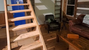 A wooden staircase leading to a door, a black leather chair, a brown leather sofa, and a small wooden table in a room with wooden floors and walls. - Historical Square Timber Home right at the heart of Snow Country (Eganville)