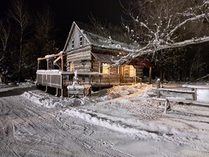 A log cabin with a porch and a snow-covered yard. - Historical Square Timber Home right at the heart of Snow Country (Eganville)
