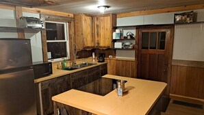 A kitchen with wooden cabinets, a stainless steel refrigerator, a microwave, and a sink. - Historical Square Timber Home right at the heart of Snow Country (Eganville)
