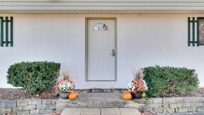 A house with a white door, two potted plants with flowers and pumpkins, and a stone wall. - Peaceful Horseheads Hideaway w/ Deck & Yard! (Horseheads)