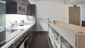 A modern kitchen with stainless steel appliances, a white countertop, and a wooden bench. - The Barrel Store is a unique hostel in the heart of the Cotswolds. (CIRENCESTER)