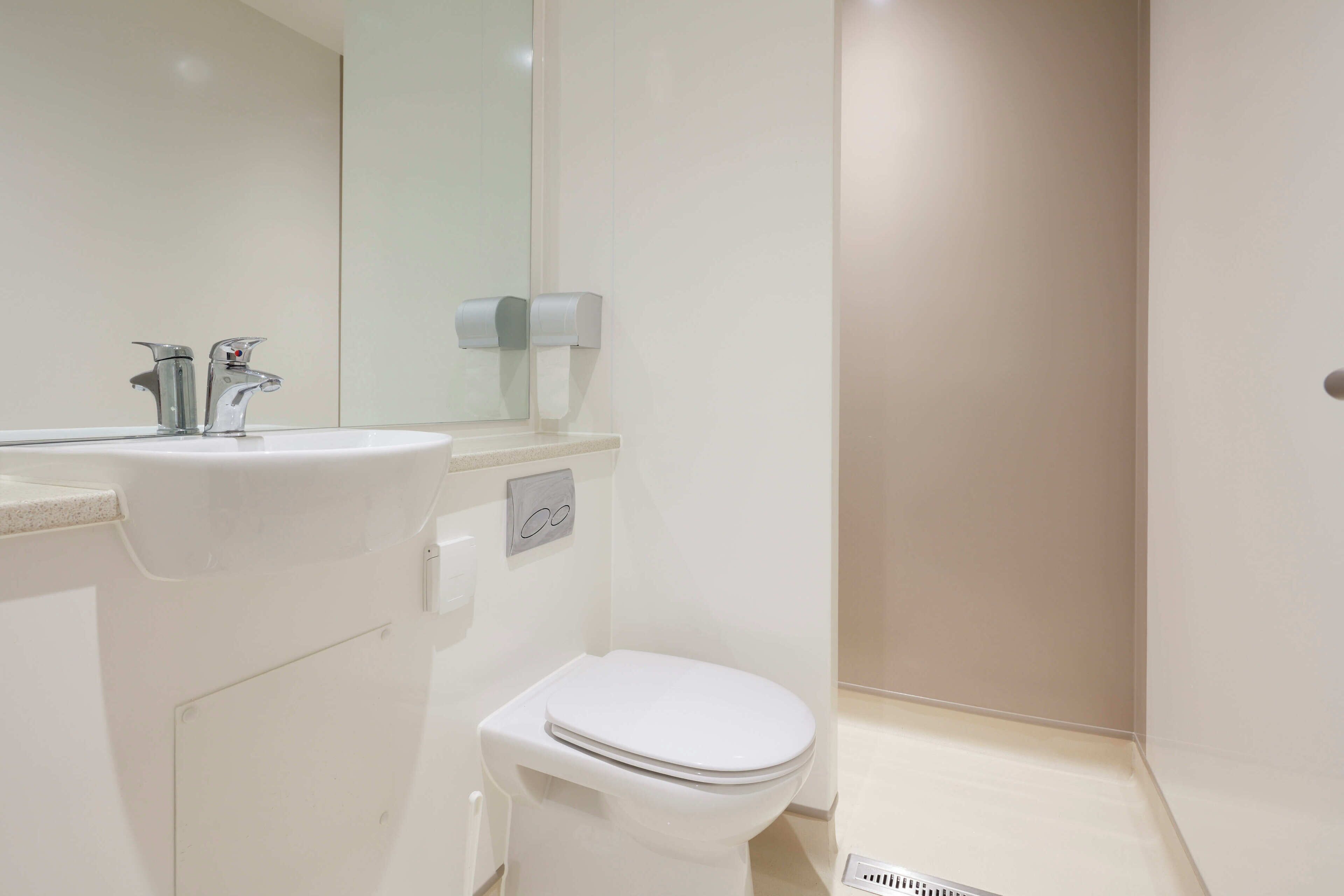 A modern bathroom with a white sink, a mirror, a toilet, and a towel dispenser.