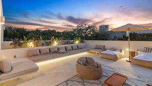Eine Dachterrasse mit einer Sofagarnitur, Sitzsäcken und einem kleinen Tisch, mit Blick auf eine Stadtlandschaft im Sonnenuntergang.