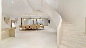 Ein geräumiger Raum mit einem zentralen Esstisch, einer geschwungenen Treppe und eingelassener Beleuchtung.