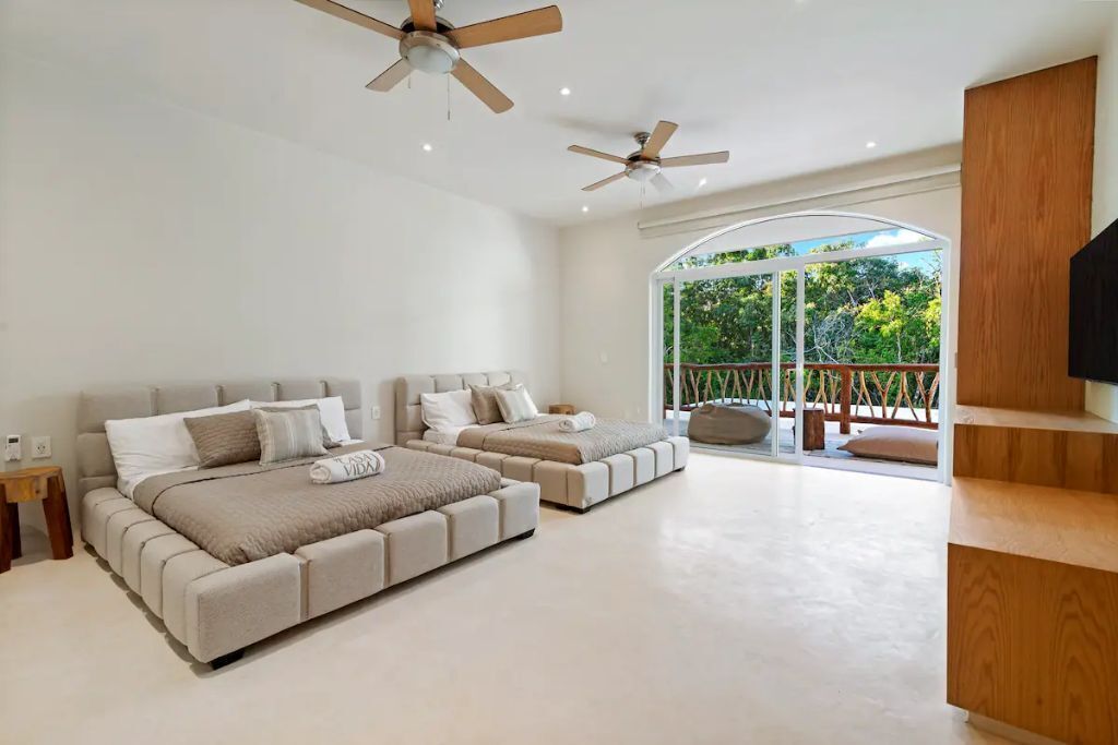 A spacious bedroom with two beds, a balcony with a view, and ceiling fans.