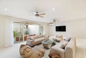 Relax in this spacious living room with a comfortable sofa set, flat-screen TV, and sliding glass door leading to an outdoor area.