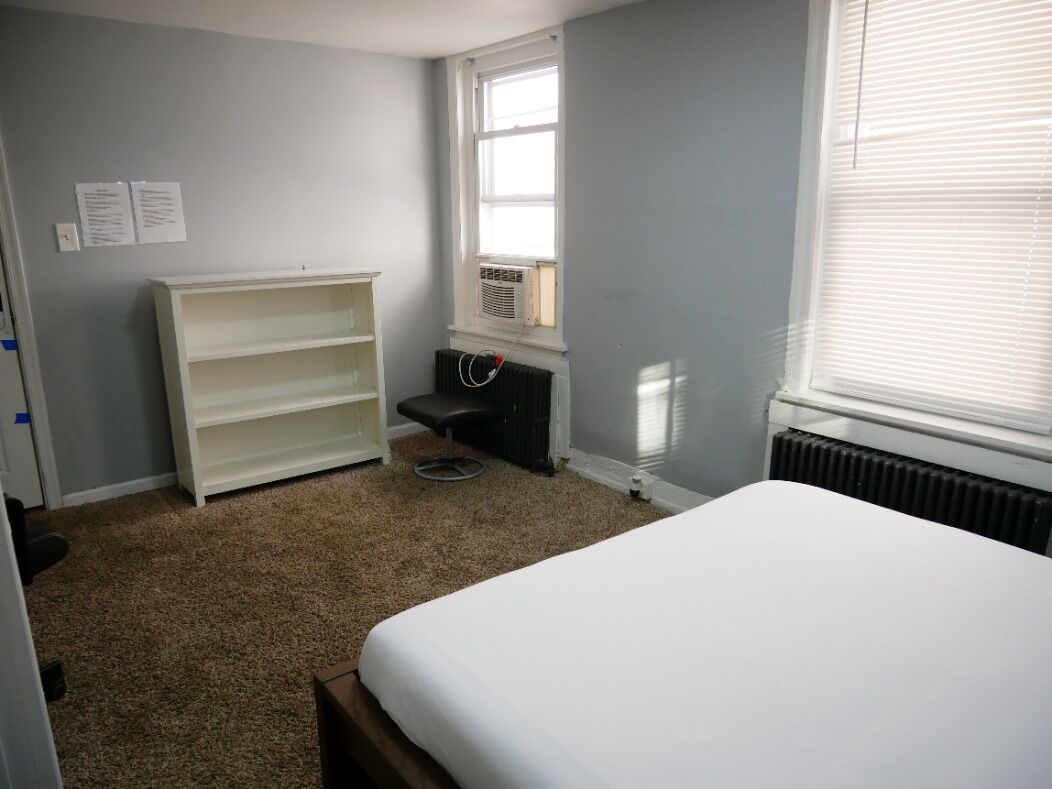 A bedroom with a bed, a white wardrobe, a radiator, and a window.