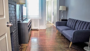 A modern living room with a dark-colored sofa, a lamp, and a fireplace. - Clover2900 Apartment & Rooms in S Philly (Philadelphia)