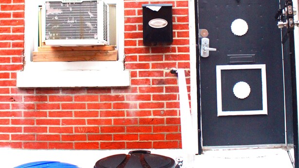 A red brick building with a black door, a window with blinds, and two trash bins labeled "Worth." - Clover2900 Apartment & Rooms in S Philly (Philadelphia)