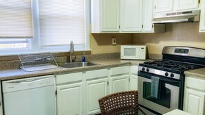 A kitchen with white cabinets, a microwave, a stove, and a dishwasher. - Clover2900 Apartment & Rooms in S Philly (Philadelphia)