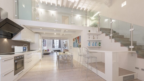 A modern kitchen with white cabinetry, a built-in oven, and a dining area with a glass table and chairs. - Le Grazie Luxury Apartment by Mmega (Florence)