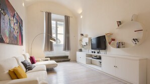 A modern living room with a white sofa, a flat-screen TV, a circular bookshelf, and a staircase leading to an upper floor. - Le Grazie Luxury Apartment by Mmega (Florence)