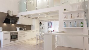 A modern kitchen with white cabinetry, stainless steel appliances, and a glass dining area. - Le Grazie Luxury Apartment by Mmega (Florence)