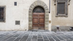 A stone building with a large wooden double door, a small window with a decorative grille, and a stone-paved entrance. - Le Grazie Luxury Apartment by Mmega (Florence)