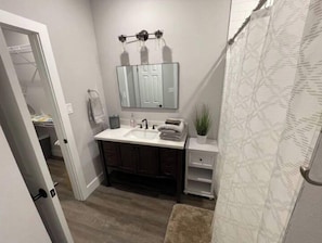 A bathroom with a white sink, dark wooden cabinets, a mirror with lights, a small plant, and a shower curtain.