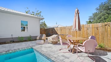 A backyard with a swimming pool, patio furniture, and a wooden fence.