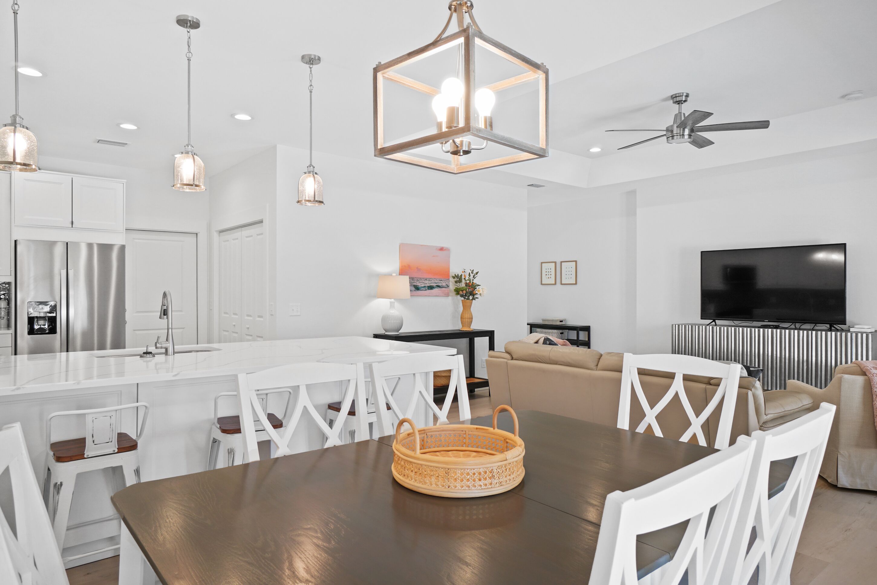 A modern kitchen with white cabinets, a stainless steel refrigerator, and a dining area with a wooden table and white chairs.