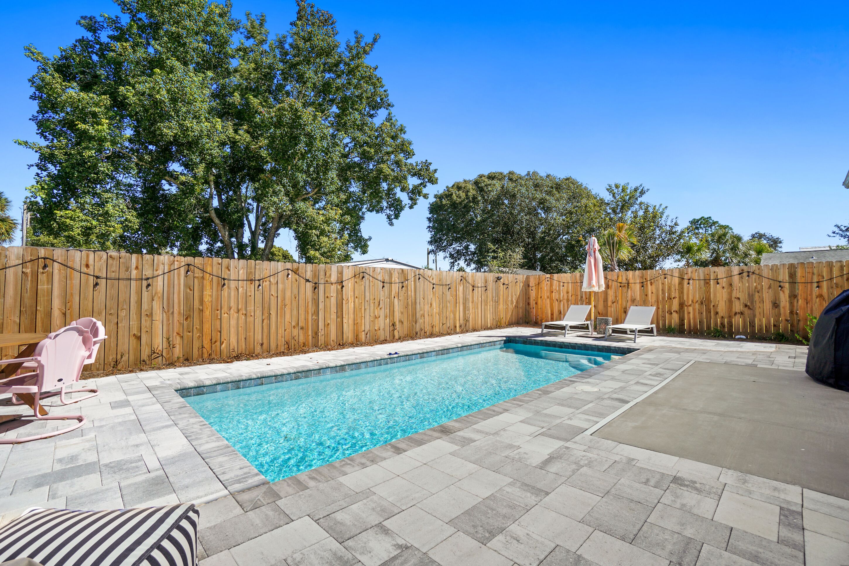 A backyard with a swimming pool, wooden fence, and lounge chairs.