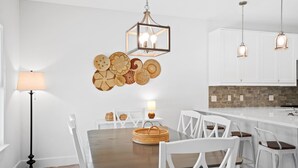 A modern kitchen with white cabinets, a wooden dining table, and a hanging light fixture. - Beach House - The Sanderling by PHG (Panama City Beach)