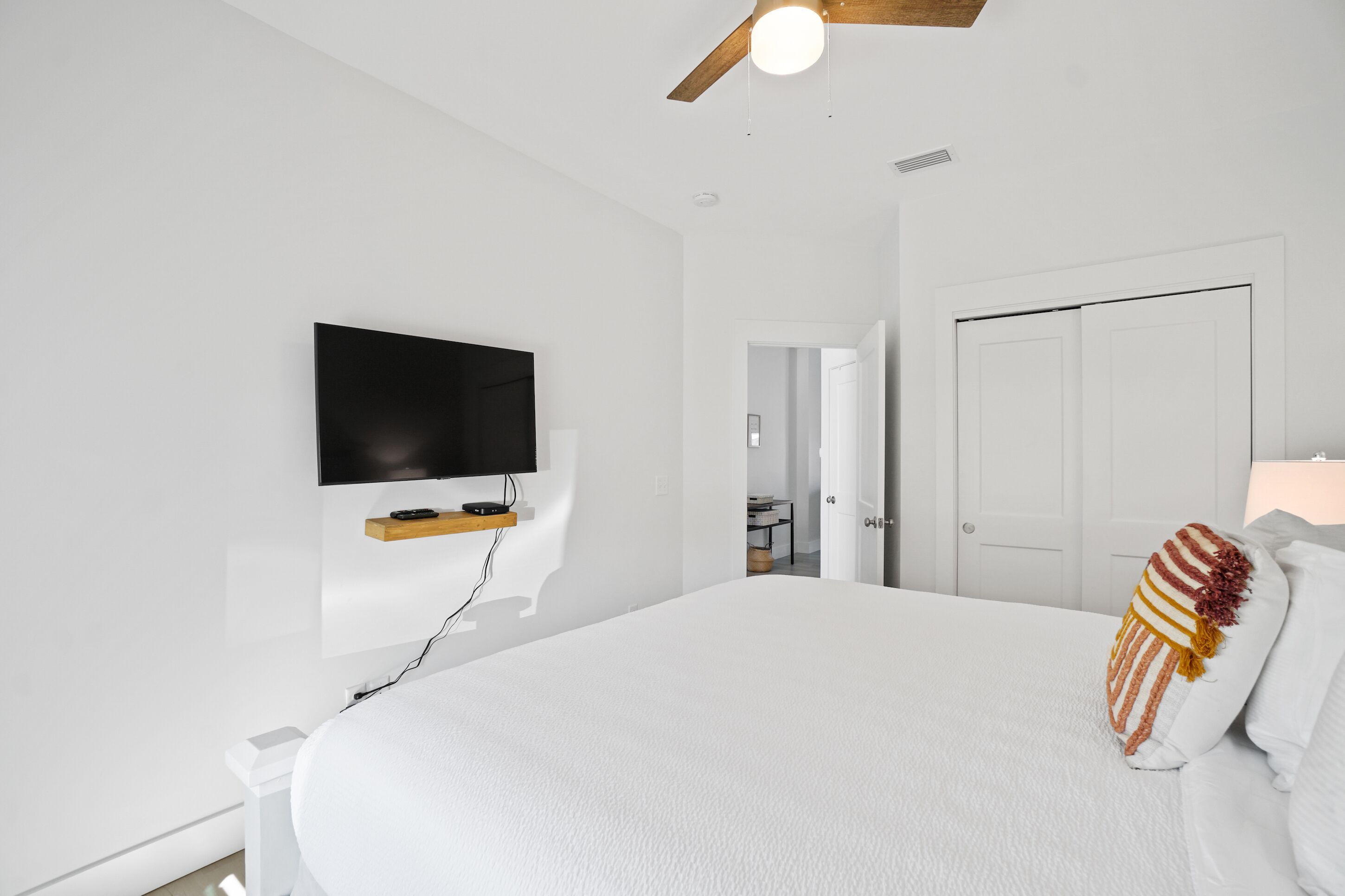 A modern bedroom with a large bed, a mounted TV, and a ceiling fan.