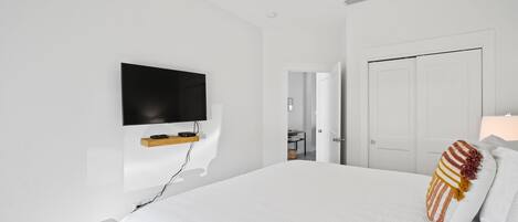 A modern bedroom with a large bed, a mounted TV, and a ceiling fan.