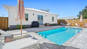 A backyard with a swimming pool, lounge chairs, and a covered barbecue area. - Beach House - The Sanderling by PHG (Panama City Beach)