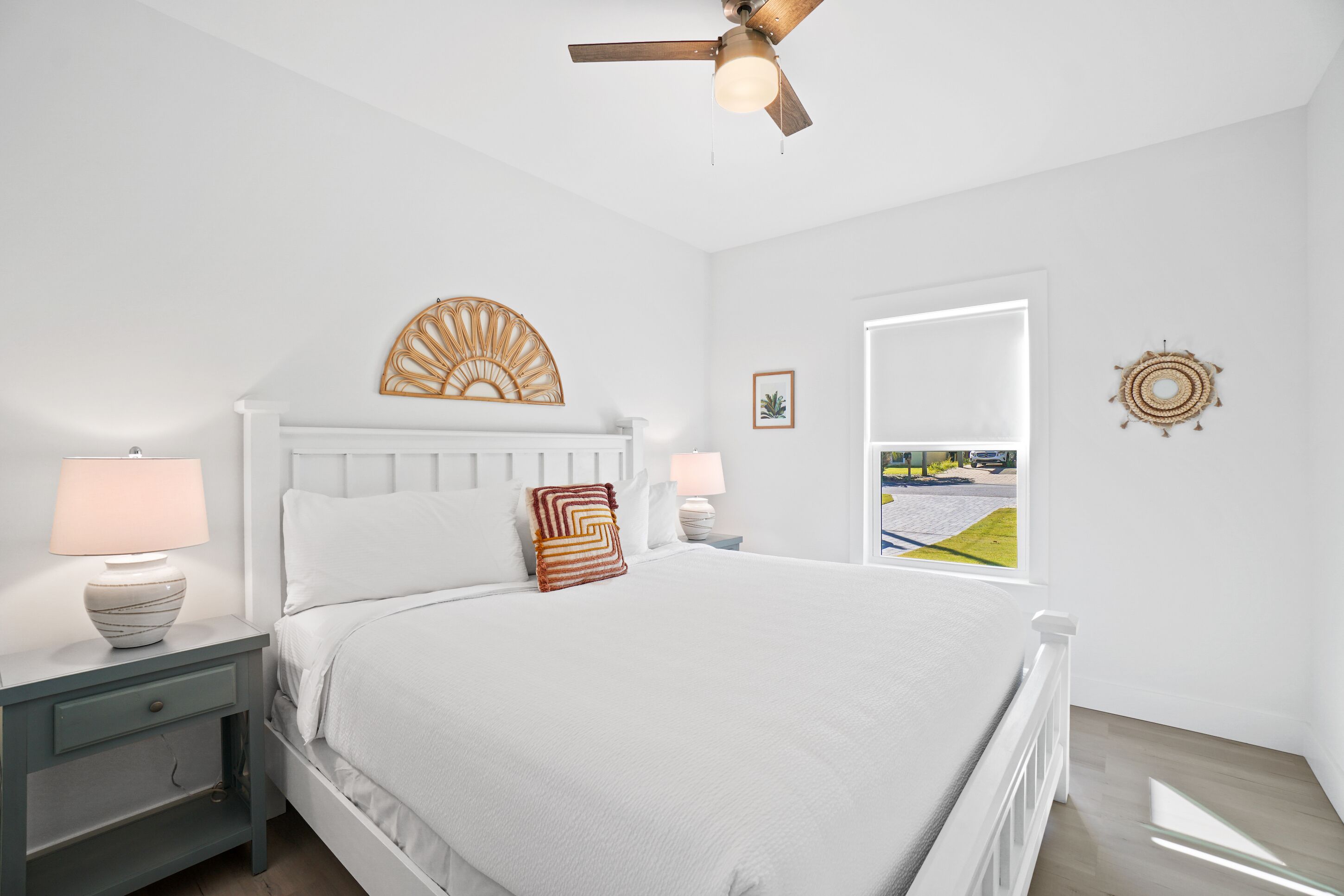 A bedroom with a bed, nightstands, a ceiling fan, a window with a view, and decorative wall art.