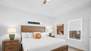 A bedroom with a wooden bed, two bedside tables with lamps, a window with a view, and a ceiling fan. - Beach House - The Sanderling by PHG (Panama City Beach)